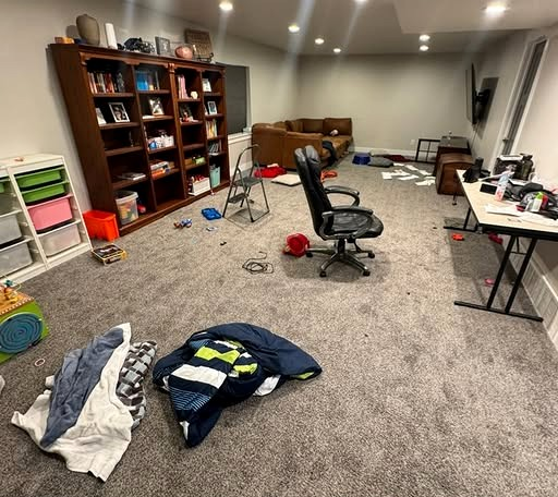 Basement before a Reset: blankets on the carpet, a crowded desk, and a room in mid-life.