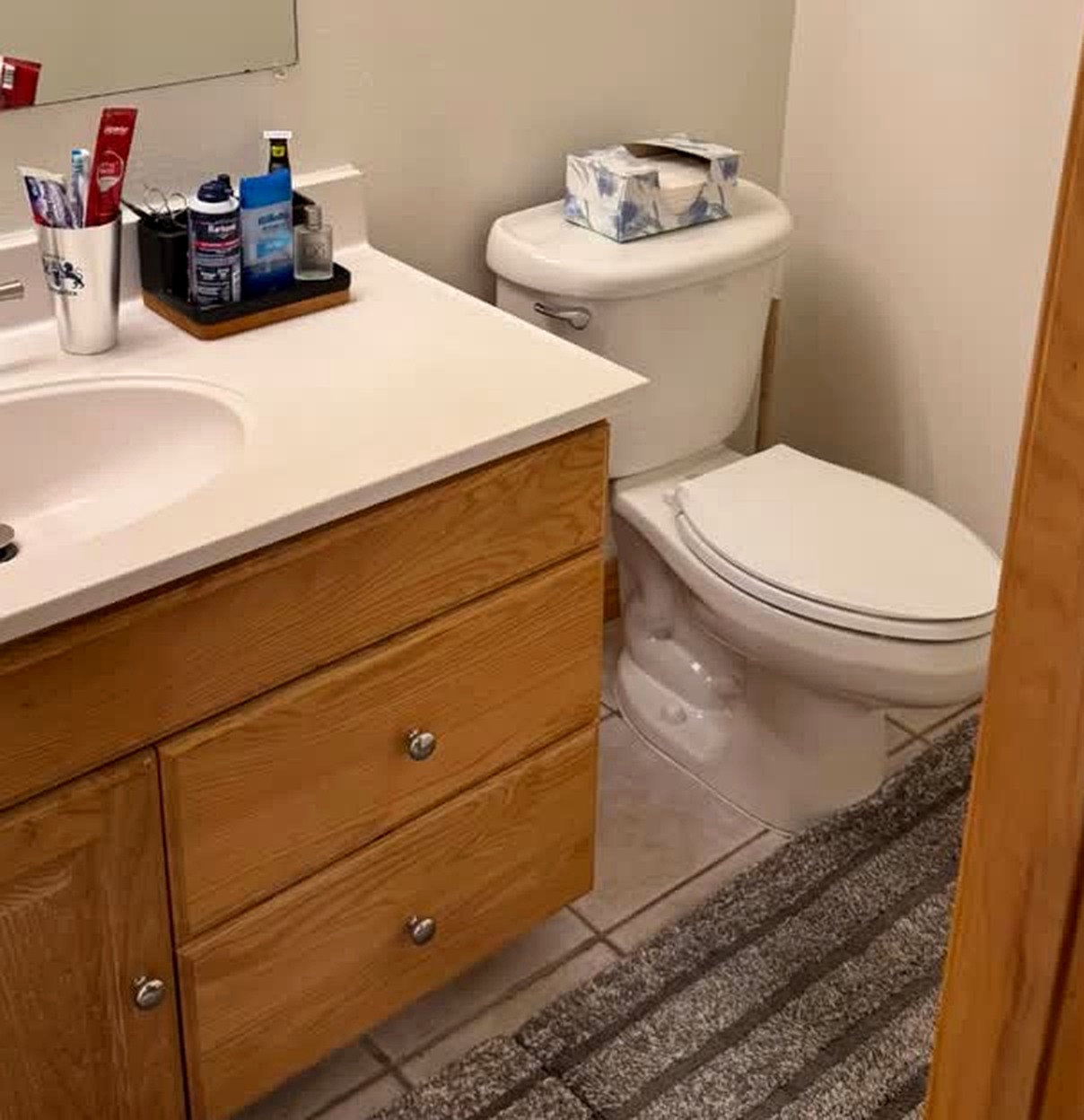 A quiet bathroom after a Reset: oak vanity, white sink, and a striped rug on clean tile.